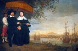 While Mathieuson and his wife dress in the demure Protestant Dutch style of the times, their overdressed slave holds a parasol, or 'pajong', above them. With his cane, the merchant indicates a fleet of ships belonging to the Dutch East India Company (VOC). In the background lies the partially walled city of Batavia, the hub of the VOC’s operations in Asia.<br/><br/>

The Dutch East India Company, or VOC, was a chartered company granted a monopoly by the Dutch government to carry out colonial activities in Asia. It was the first multinational corporation in the world and the first company to issue stock. It was also arguably the world's first megacorporation, possessing quasi-governmental powers, including the ability to wage war, imprison and execute convicts, negotiate treaties, coin money and establish colonies.<br/><br/>

The VOC was set up in 1602 to gain a foothold in the East Indies (Indonesia) for the Dutch in the lucrative spice trade, which until that point was dominated by the Portuguese.<br/><br/>

Between 1602 and 1796, the VOC sent almost a million Europeans to work in the Asia trade on 4,785 ships, and netted more than 2.5 million tons of Asian trade goods.